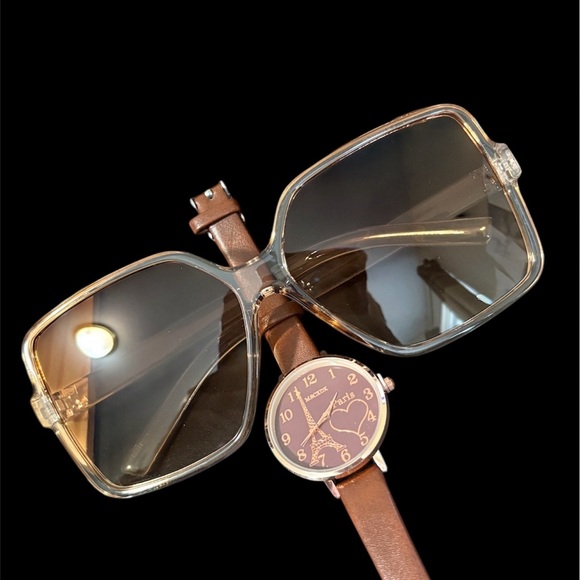 A brown leather strap watch with a heart-shaped dial and sunglasses.